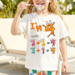 May include: White t-shirt with the text "I'M 4" and math equations featuring animated numbers. The shirt has a colorful design with orange, pink, yellow, and blue accents. The child is holding a bubble wand.