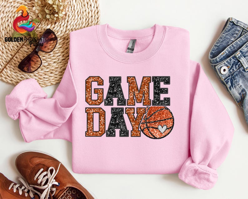 May include: Pink sweatshirt with a glittery orange and black "GAME DAY" graphic and a basketball with a heart on it.