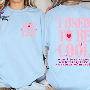 May include: Light blue sweatshirt with pink text that reads "I USED TO BE COOL now I just argue with miniature versions of myself" with a pink heart in the text.