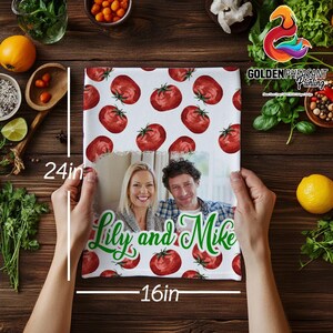May include: A personalized kitchen towel, 24 x 16 inches, featuring a repeating pattern of red tomatoes. The bottom half displays a photo of a smiling couple, with the names "Lily and Mike" in green script. The towel is held by hands.