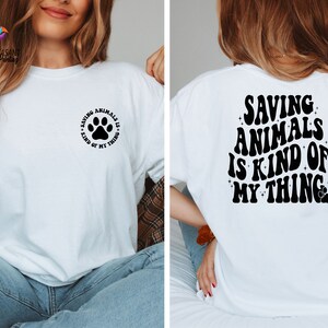 May include: White t-shirt with a black paw print and the text "Saving Animals is Kind of My Thing" on the front. The back of the shirt has the text "Saving Animals is Kind of My Thing" in a retro font with a paw print.