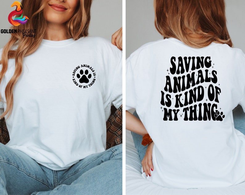 May include: White t-shirt with a black paw print and the text "Saving Animals is Kind of My Thing" on the front. The back of the shirt has the text "Saving Animals is Kind of My Thing" in a retro font with a paw print.