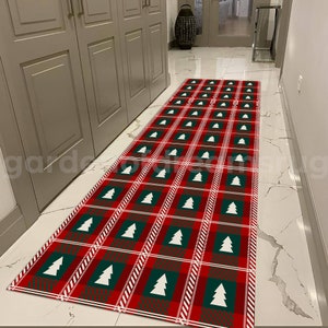 May include: A red and green plaid runner rug with white Christmas trees. The rug is in a hallway with white tile floors.