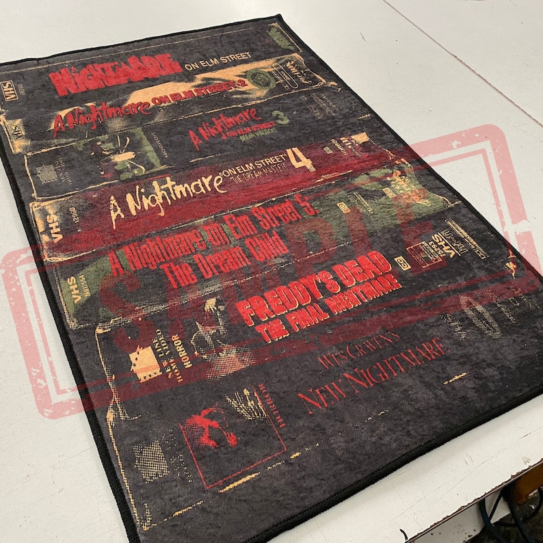 May include: A black and red rug with a design of VHS tapes featuring the movie titles "A Nightmare on Elm Street" and "Freddy's Dead: The Final Nightmare".