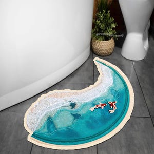 May include: A crescent-shaped bath mat with a blue ocean wave design and two red fish swimming in the water. The mat has a white border.