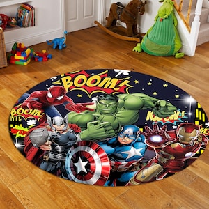 Puede incluir: Alfombra redonda con fondo azul que presenta una imagen de estilo cómic de superhéroes, incluyendo Spiderman, Hulk, Thor, Capitán América y Iron Man. La alfombra tiene las palabras "BOOM!" y "Kapow!" impresas en ella.