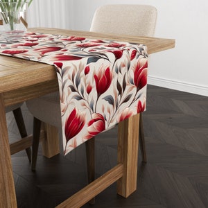 May include: A floral table runner with a cream background and red, pink, and blue flowers. The runner is on a wooden table with a chair.