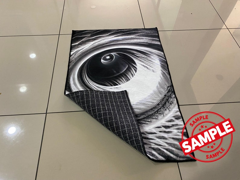 May include: Black and white rug with a large eye design. The rug has a black and white checkered backing.