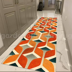 Könnte beinhalten: Ein geometrisch gemusterter Läufer in Orange-, Grün- und Grautönen. Der Läufer liegt in einem Flur mit weißen Fliesen.