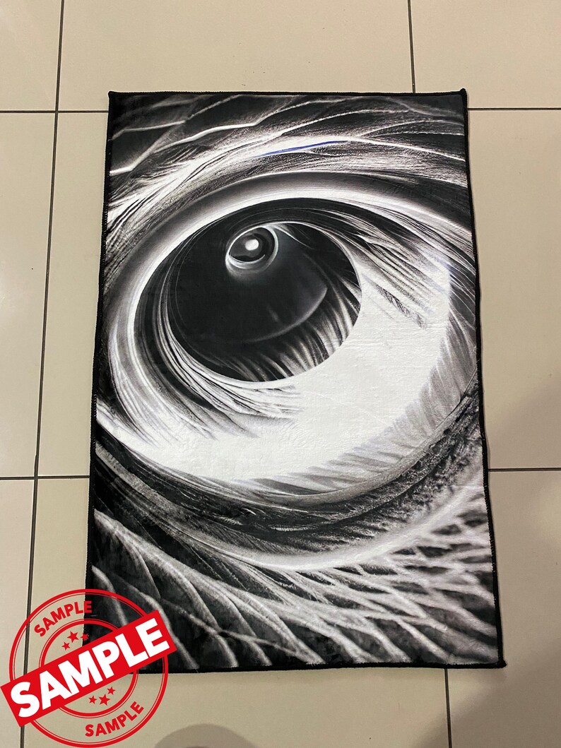 May include: Black and white abstract rug with a large eye-like design. The rug has a soft, plush texture.