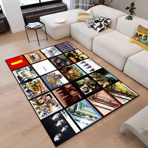Puede incluir: Una alfombra negra y blanca con un diseño de portada de álbum de los Beatles. La alfombra presenta portadas de álbumes de la discografía de los Beatles, incluyendo "Sgt. Pepper's Lonely Hearts Club Band", "Abbey Road" y "Rubber Soul".