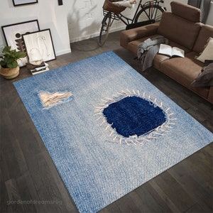 May include: A blue and white distressed denim rug with a large hole in the center, stitched with white thread. The rug has a faded denim look and is perfect for adding a casual and trendy touch to any room.