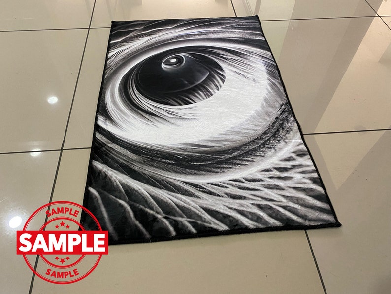May include: Black and white abstract rug with a large eye design. The eye is surrounded by swirling lines and patterns.