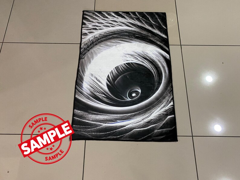 May include: Black and white abstract rug with a swirling design that resembles an eye. The rug has a soft, plush texture.