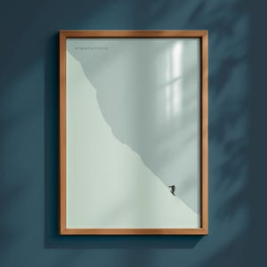 May include: Framed print with a minimalist design of a skier on a mountain slope. The artwork has a light green and grey colour palette, with a brown wooden frame. Coordinates are printed in the upper left corner.