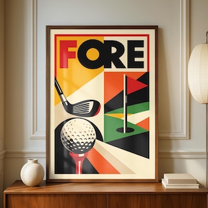 May include: A framed art print with a golf theme. The word "FORE" is in large red and black letters at the top. Below, a golf ball sits on a tee, with a golf club and a red flag on a green. The background has orange, yellow, and black geometric shapes.