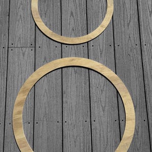 May include: Two wooden hoops, one larger than the other, are placed on a gray wood surface. The hoops are both natural wood color.