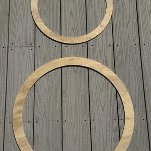 May include: Two wooden hoops, one larger than the other, are placed on a gray wooden surface. The hoops are both made of light brown wood and have a smooth finish.