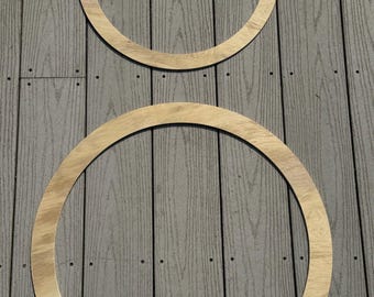 May include: Two wooden hoops, one larger than the other, are placed on a gray wooden surface. The hoops are both made of light brown wood and have a smooth finish.