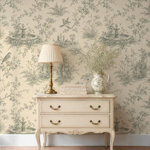 May include: A cream-colored wooden dresser with two drawers, topped with a pleated lampshade on a brass base, a floral ceramic pitcher, and three stacked books titled Maison de Campagne, French Country Living, and The Gardens of France.