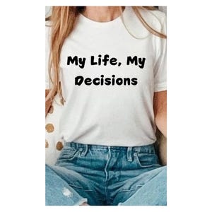 以下が含まれることがあります： 黒い文字で「My Life, My Decisions」とプリントされた白いTシャツ