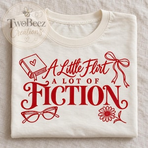 Peut inclure: Un t-shirt couleur crème avec un texte graphique rouge qui indique A Little Flirt A LOT OF FICTION. Le motif comprend des illustrations d'un livre avec un cœur, un ruban, des lunettes œil-de-chat et une fleur. Le logo TwoBeez Creations est visible.