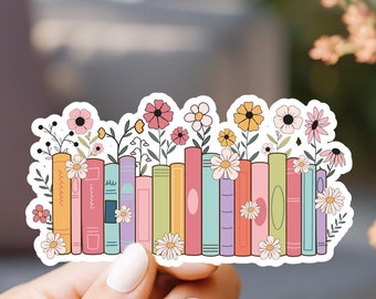 May include: A sticker featuring a row of colorful books with flowers growing out of the top. The books are arranged vertically and have different colors and patterns. The flowers are pink, yellow, and white.