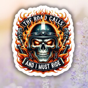 May include: A sticker featuring a skull wearing a motorcycle helmet, surrounded by flames. The text reads "THE ROAD CALLS AND I MUST RIDE". The design is in shades of black, orange, and white, with a bold, graphic style.