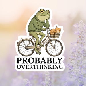 May include: A sticker featuring a cartoon frog riding a bicycle, wearing a green sweater, and resting its chin on its hand. A small orange cat sits in the front basket. The text "PROBABLY OVERTHINKING" is below the image.