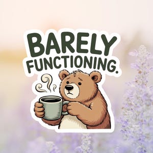 May include: A sticker featuring a cartoon bear holding a coffee mug. The bear has a tired expression and the text "Barely Functioning" above it. The sticker is brown, white, and green, set against a blurred floral background.