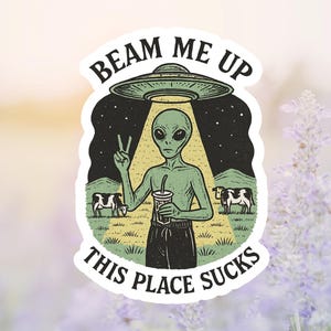 May include: A sticker featuring an alien under a UFO with the text "Beam Me Up This Place Sucks." The alien is green, holding a drink, and making a peace sign. Cows graze in the background.
