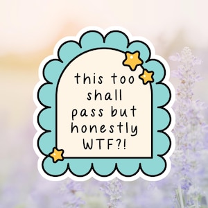 May include: A sticker with a light blue scalloped border and a cream-colored interior. The sticker has the text "this too shall pass but honestly WTF?!" with two yellow star accents. The background is a blurred image of purple flowers.