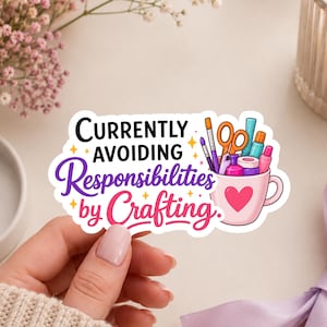 May include: A die-cut sticker featuring a pink mug filled with various craft supplies like scissors, brushes, and glue. The text reads Currently AVOIDING Responsibilities by Crafting. The design includes small yellow stars and a pink heart on the mug.