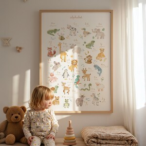 Sweet toddler girl in pajamas sitting on the floor next to a teddy bear and wooden toy pyramid, looking at a large framed watercolor animal alphabet chart hanging on a sunlit nursery wall. Warm, aesthetic scandinavian style playroom.