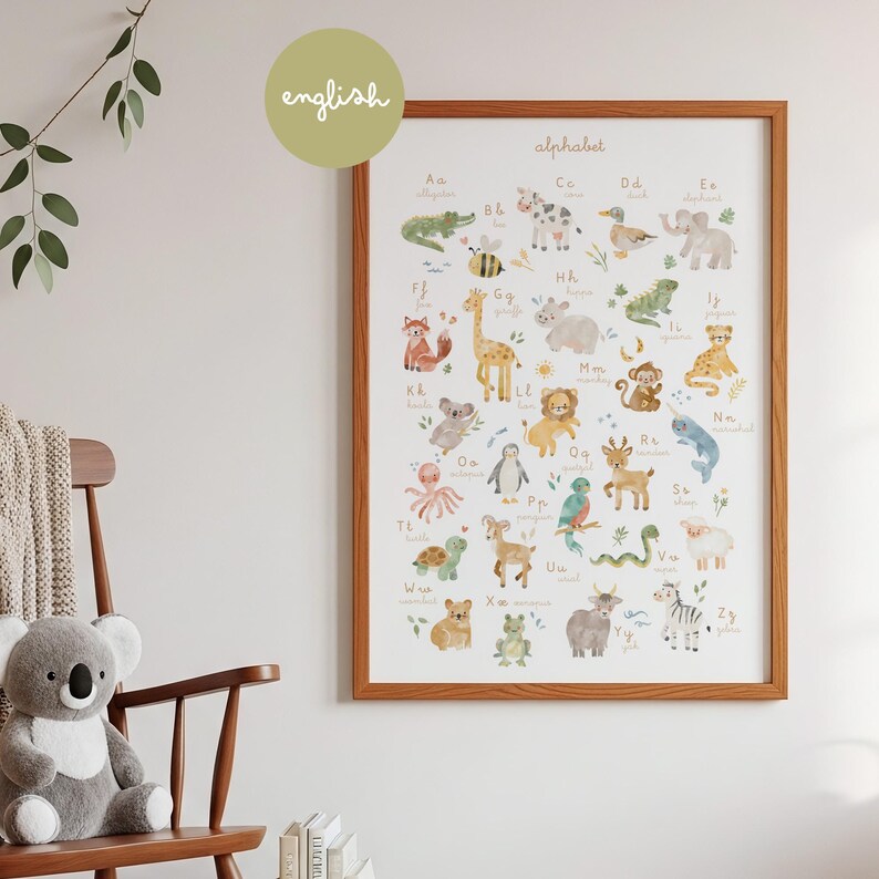 Cozy nursery room decor mockup featuring the watercolor alphabet poster framed on a neutral wall. Next to a wooden rocking chair with a plush koala teddy bear, green leaves, and natural warm lighting. Perfect gender-neutral kids bedroom wall decor.