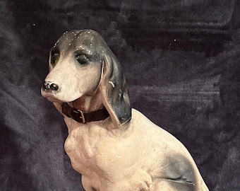 May include: A white and black ceramic dog figurine sitting on a wooden base. The dog is wearing a brown leather collar.