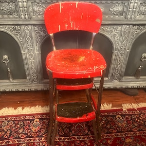 May include: A red step stool with a black top step. The stool has a metal frame and is in a worn condition.