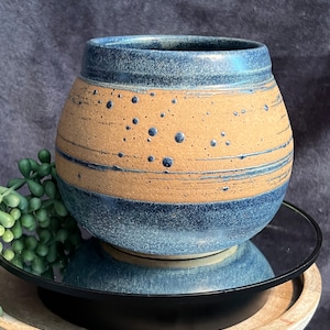 May include: A blue and brown ceramic planter with a speckled glaze. The planter has a rounded shape and a wide opening.