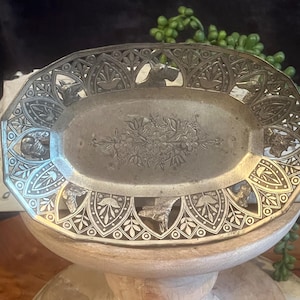 May include: A silver oval-shaped dish with an intricate design featuring a floral motif and small animal figures around the edge. The dish is made of metal and has a shiny finish.