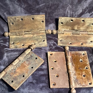 May include: Four antique brass hinges with decorative ball finials. The hinges are in various states of wear and patina, showing signs of age and use.