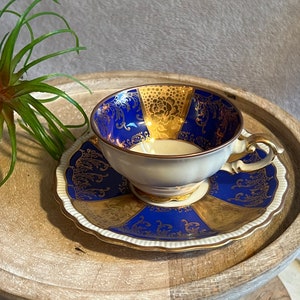 May include: A blue and gold teacup and saucer set with a floral design. The cup and saucer are made of porcelain and have a delicate, ornate pattern.