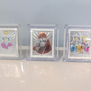 May include: Three framed silver religious icons. The icons are in clear plastic cases. The first icon has a yellow and pink design. The second icon has a figure with an orange head covering. The third icon has a multi-colored design.