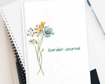 May include: A white journal with a watercolor illustration of blue and yellow flowers. The text "Garden Journal" is written in green on the front cover.