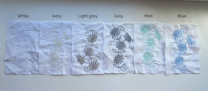 May include: A collection of white linen fabric swatches, each embroidered with a floral design in various colors. The colors include white, ivory, light grey, grey, mint, and blue. The text above each swatch indicates the color.