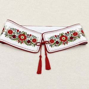 May include: A white detachable collar featuring intricate floral embroidery in shades of red, dark red, and green. The collar has a red piped edge and is secured at the front with a thin red cord ending in two matching decorative tassels.