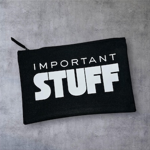 May include: A black rectangular pouch with a zip closure. The words "IMPORTANT STUFF" are printed in large white capital letters across the front. The pouch is made of fabric.