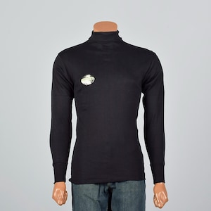 May include: Black long-sleeve turtleneck shirt with a small, circular emblem on the chest. The shirt has a close fit and is made of a smooth fabric. The sleeves end with ribbed cuffs. The mannequin is wearing blue jeans.