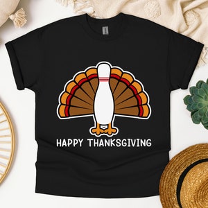 Op de afbeelding: Zwart T-shirt met een wit bowlingpin-kalkoenontwerp en de tekst "Happy Thanksgiving".