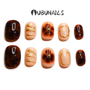 Short almond-shaped handmade press-on nails in ombre brown and peach gold tones. 3D gel design features free-style sculpted flowers, giving a delicate and elegant look. The nails have a clean, simple finish, perfect for daily wear or special occasions like birthday partiy. Subtle shimmer adds a festive touch, making them an ideal gift for her. Displayed neatly in a set, highlighting the smooth glossy texture and intricate floral details. Suitable for OOTD styling or gifting as a birthday present