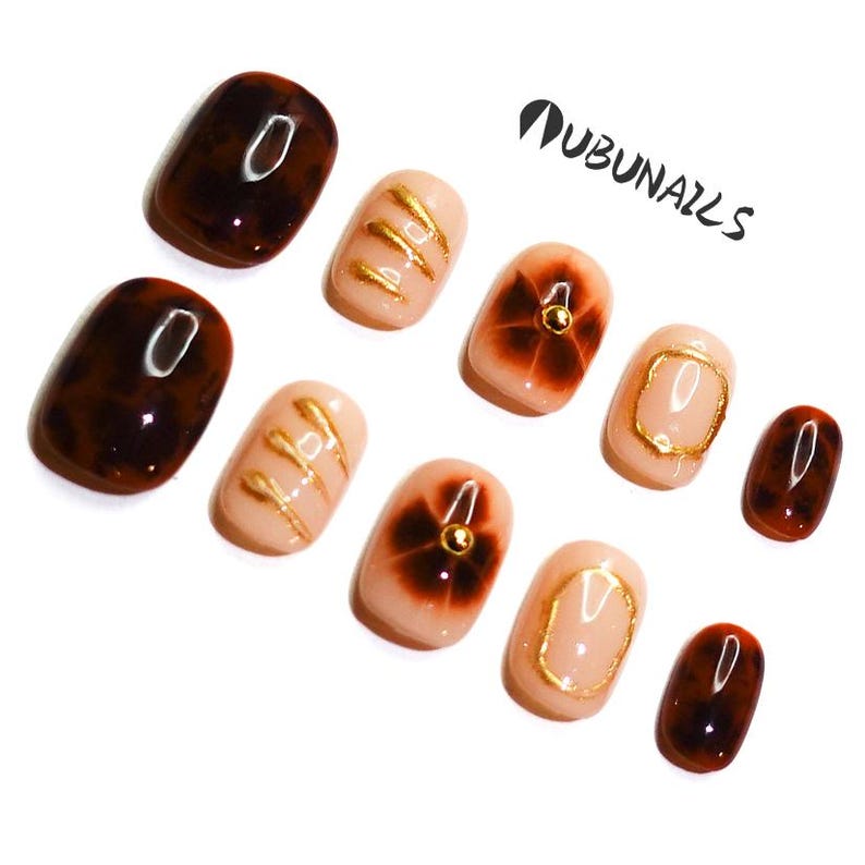 Short almond-shaped handmade press-on nails in ombre brown and peach gold tones. 3D gel design features free-style sculpted flowers, giving a delicate and elegant look. The nails have a clean, simple finish, perfect for daily wear or special occasions like birthday partiy. Subtle shimmer adds a festive touch, making them an ideal gift for her. Displayed neatly in a set, highlighting the smooth glossy texture and intricate floral details. Suitable for OOTD styling or gifting as a birthday present